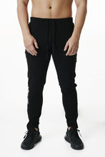 Load image into Gallery viewer, A man standing wearing True form Statement Collection Black Tapered Joggers

