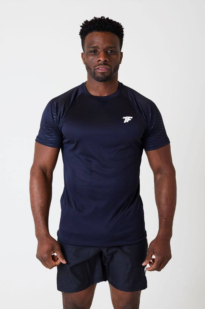 A man standing facing front wearing true form black embossed T-shirt