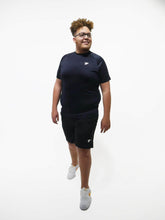 Load image into Gallery viewer, A man standing facing front wearing black embossed T-shirt with shorts of brand true form uk
