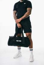 Load image into Gallery viewer, A man holding a black bag wearing true form black T-shirt and black shorts
